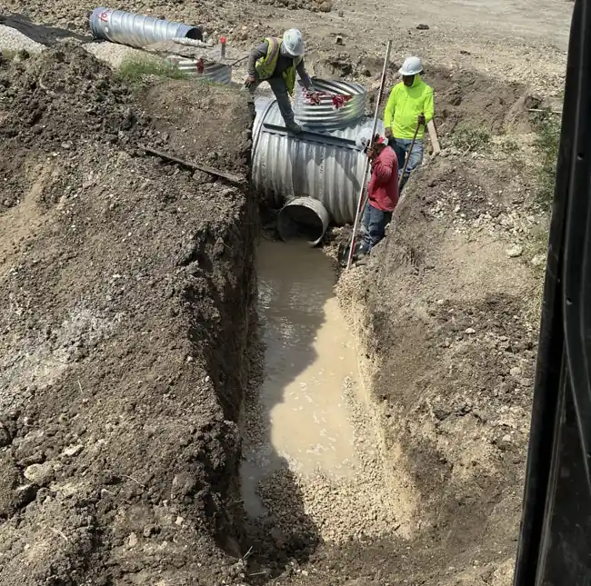 Crew installing a corrugated metal underground detention tank in a trench