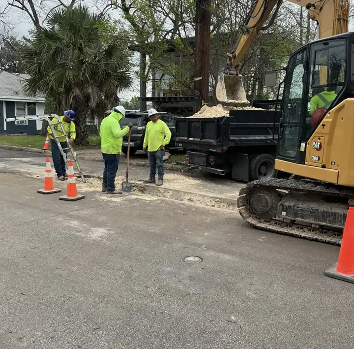 Aqua Clear Utilities crew working an open street cut with a CAT 308 excavator loading spoils into a dump truck