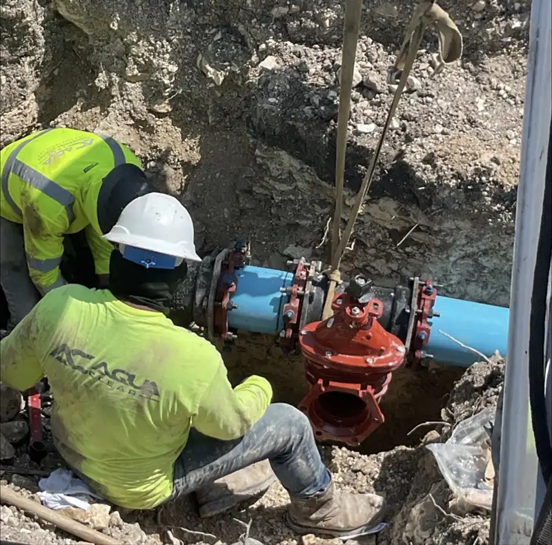 Aqua Clear Utilities crew installing a red fire line valve assembly on a blue underground fire line in an open trench