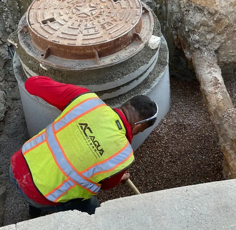 Aqua Clear Utilities crew member setting the cast-iron ring and cover on a precast concrete manhole