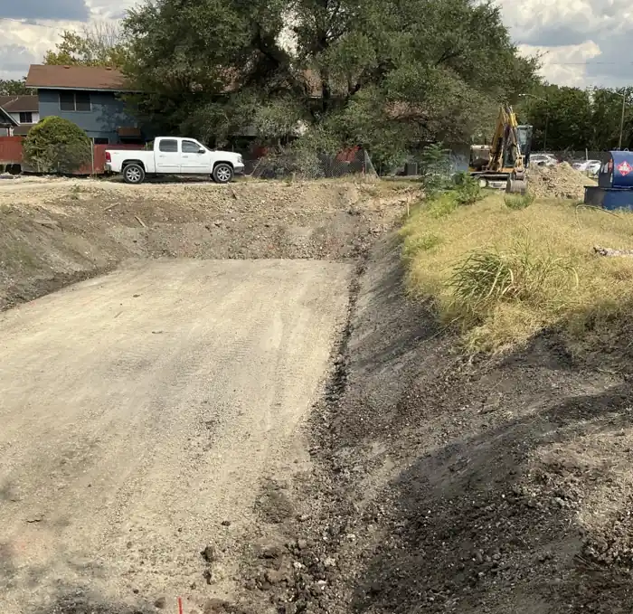 Excavated stormwater pond basin graded to plan on a Texas job site, with an excavator working the bank