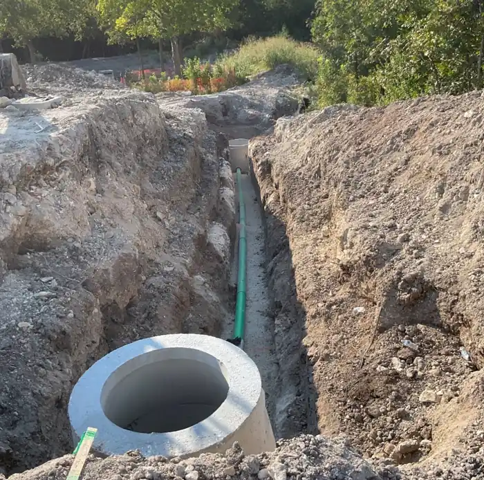 Green sewer line running through an open trench between precast concrete manholes
