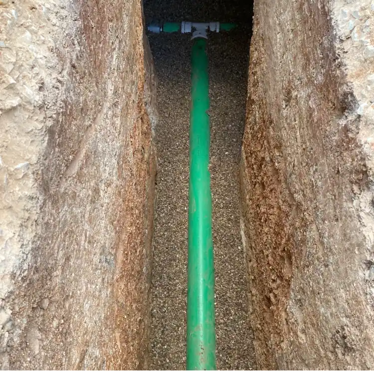 Green sewer pipe laid in a gravel-bedded trench, joined at a tee fitting