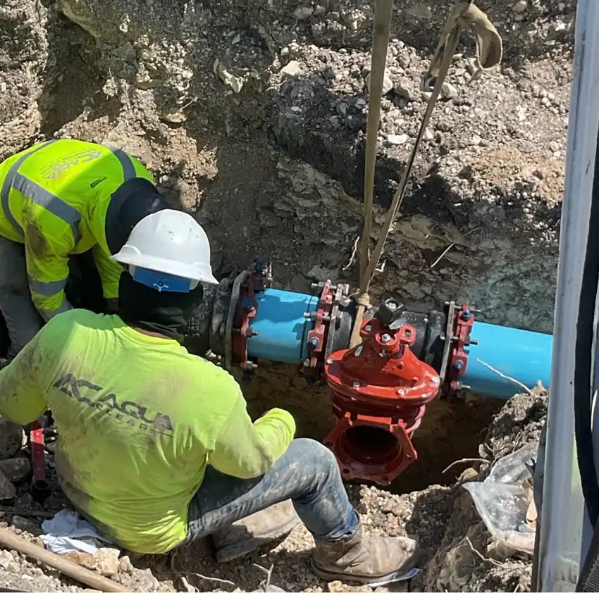 Aqua Clear Utilities crew installing a blue water main with a red valve fitting in an open trench