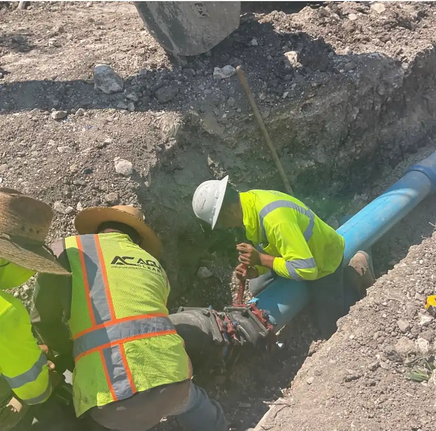 Aqua Clear Utilities crew lowering a blue water pipe into an open trench and bolting up the fitting
